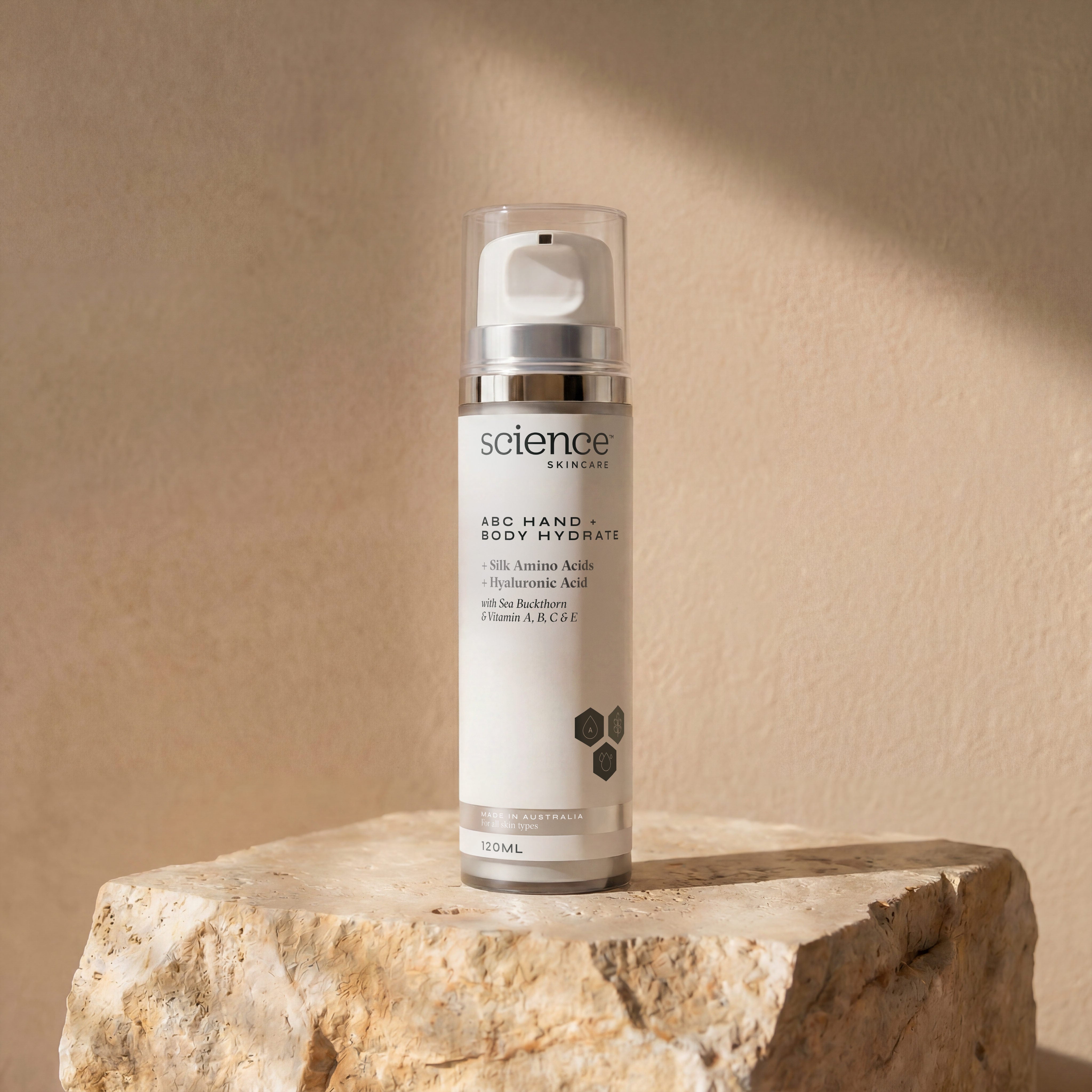 ABC Hand + Body Hydrate lifestyle image showing the 120ml Science Skincare body moisturiser with silk amino acids, hyaluronic acid, sea buckthorn and vitamins A, B, C and E, styled on a raw stone plinth with natural shadow play
