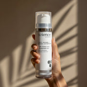 ABC Hand + Body Hydrate lifestyle image showing a hand holding the 120ml Science Skincare body moisturiser with silk amino acids, hyaluronic acid, sea buckthorn and vitamins A, B, C and E, against a warm wall with dappled palm shadow play
