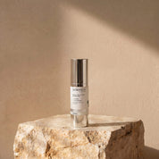 Enlighten Serum lifestyle image showing a hand holding the 30ml Science Skincare brightening serum with peptides, niacinamide, Song-yi mushroom and licorice, against a warm wall with dappled light shadows
