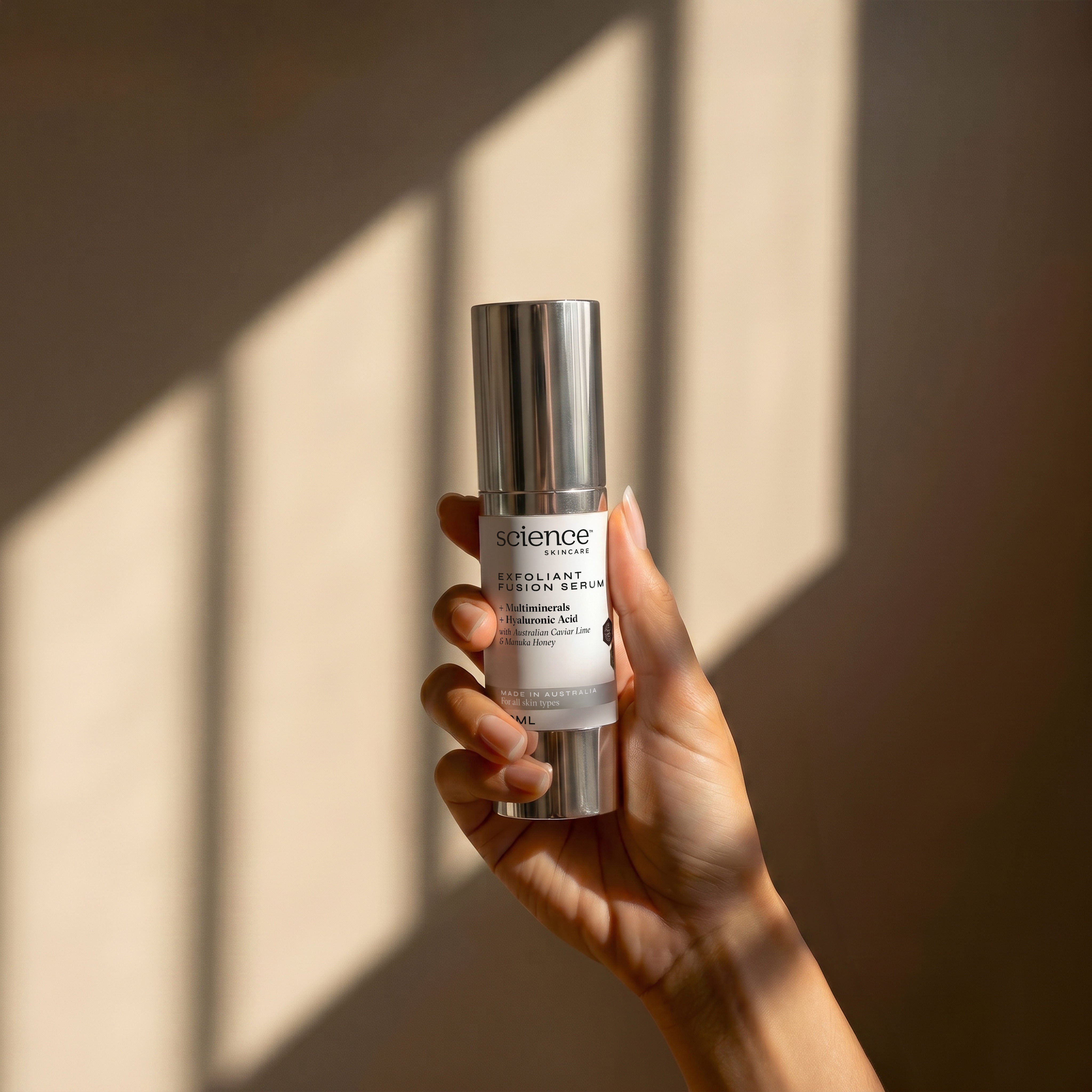 Exfoliant Fusion Serum lifestyle image showing a hand holding the 30ml Science Skincare exfoliating serum with multiminerals, hyaluronic acid, Australian caviar lime and manuka honey, against a warm wall with geometric light shadows