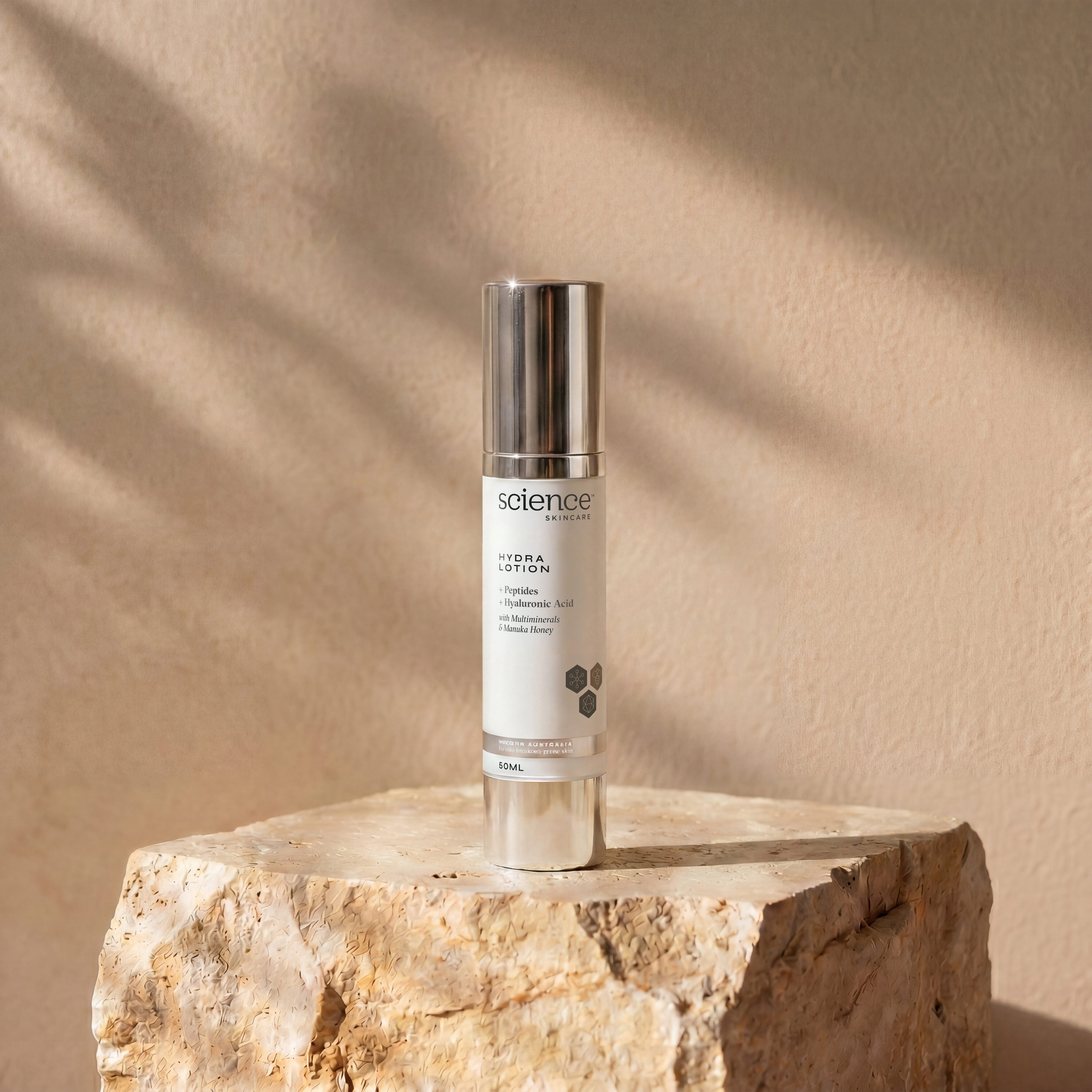 Hydra Lotion lifestyle image showing the 50ml Science Skincare lightweight moisturiser with peptides, hyaluronic acid, multiminerals and manuka honey, styled on a raw stone plinth with natural palm shadow play