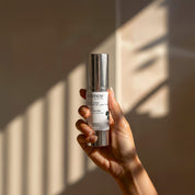 Nurture + Repair Lotion lifestyle image showing a hand holding the 30ml Science Skincare soothing lotion with peptides, hyaluronic acid, cucumber and watermelon, against a warm wall with geometric light shadows