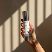 Suntint Protect Light SPF-25 lifestyle image showing a hand holding the 50ml Science Skincare tinted sunscreen with zinc, peptides, chamomile and niacinamide, against a warm wall with geometric light shadows
