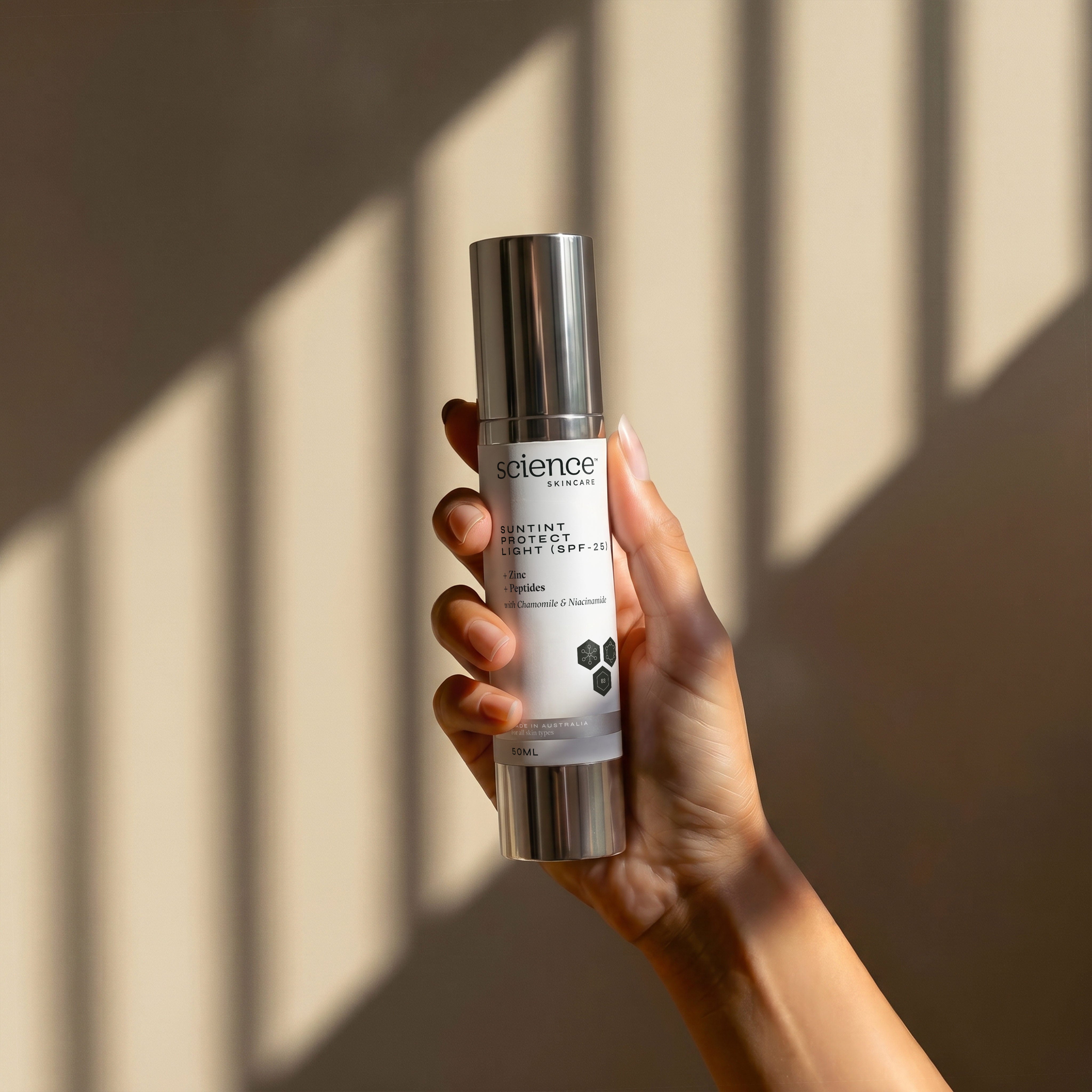 Suntint Protect Light SPF-25 lifestyle image showing a hand holding the 50ml Science Skincare tinted sunscreen with zinc, peptides, chamomile and niacinamide, against a warm wall with geometric light shadows