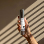 Suntint Protect Medium SPF-25 lifestyle image showing a hand holding the 50ml Science Skincare tinted sunscreen with zinc, peptides, chamomile and niacinamide, against a warm wall with diagonal light shadows
