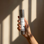 Suntint Protect Ultra Light SPF-25 lifestyle image showing a hand holding the 50ml Science Skincare tinted sunscreen with zinc, peptides, chamomile and niacinamide, against a warm wall with geometric light shadows
