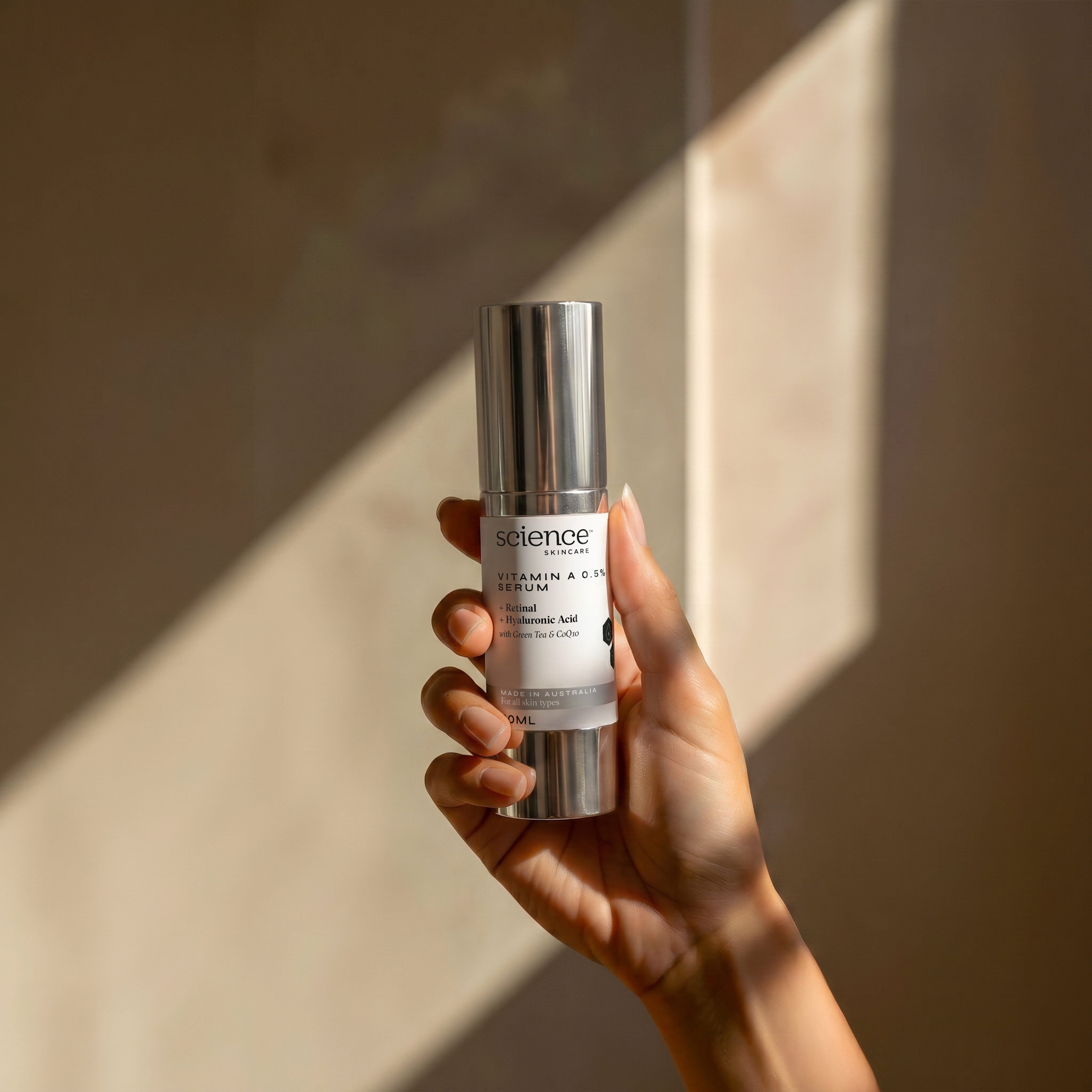 Vitamin A 0.5% Serum lifestyle image showing a hand holding the 30ml Science Skincare retinal serum with retinal, hyaluronic acid, green tea and CoQ10, against a warm wall with angular light shadows
