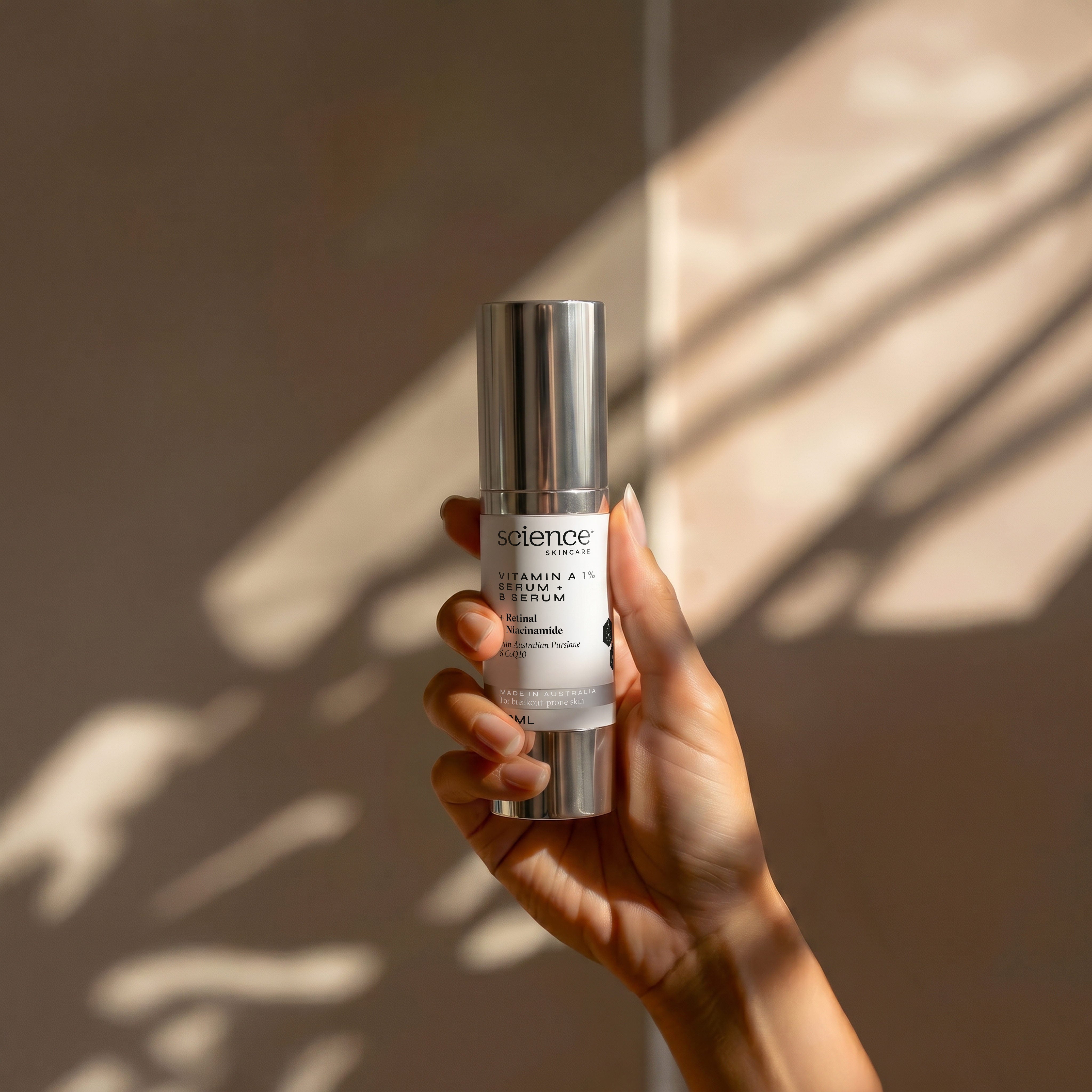 Vitamin A 1% Serum + B Serum lifestyle image showing a hand holding the 30ml Science Skincare serum with retinal, niacinamide, Australian purslane and CoQ10, against a warm wall with dappled light shadows
