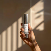 Vitamin A 1% Serum lifestyle image showing a hand holding the 30ml Science Skincare retinal serum with retinal, hyaluronic acid, green tea and CoQ10, against a warm wall with geometric light shadows
